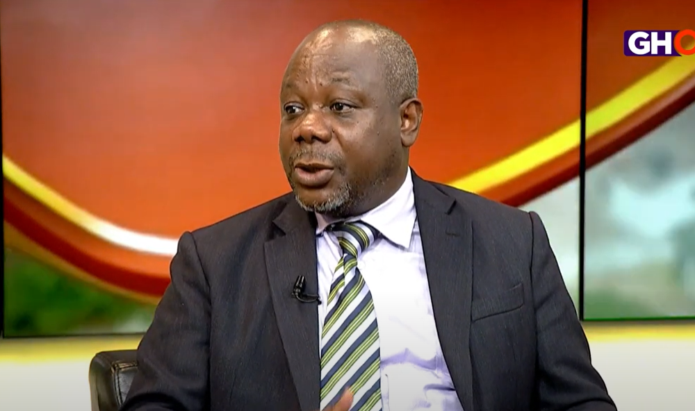 A professional portrait of lawyer Theophilus Dzimega during a television interview
